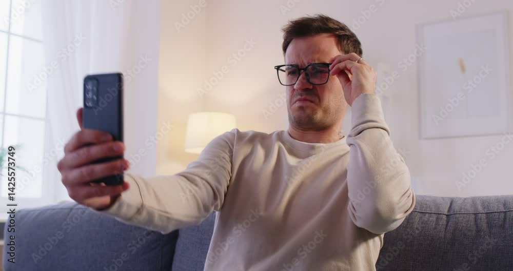 Young man wearing eyeglasses trying to read message on his smartphone having farsightedness eye disease. Male person with presbyopia looking at mobile phone screen. Vision problems concept. 4k video.