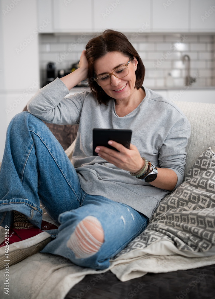 Obraz premium Girl Reading E-Book On Sofa At Home