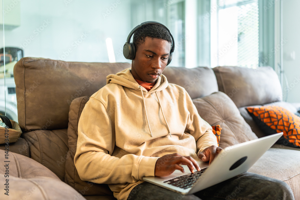 Focused young man working from home using laptop and headphones on the couch