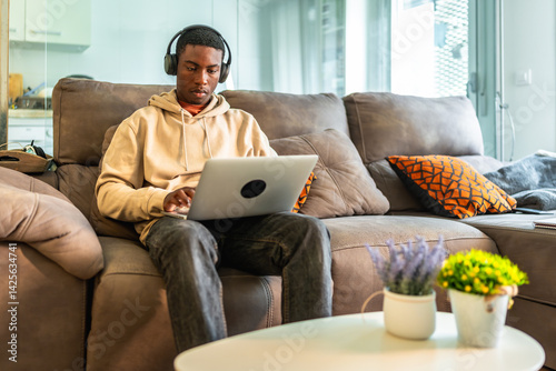 Obraz na płótnie Focused teenager working on laptop with headphones on comfortable sofa at home w salonie