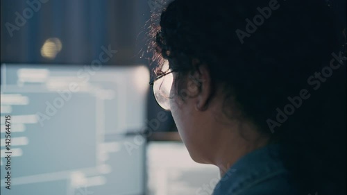 Close-up view of a female software engineer working at night, focused on glowing screen filled with code. Glasses reflecting text, symbolizing deep concentration.