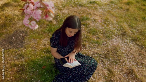 Young woman closes her Bible and smiles with joy, sitting under blooming sakura trees. A peaceful, spiritual moment surrounded by nature, faith, and the beauty of God’s word.