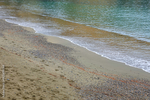 Obraz na płótnie A serene shoreline features a mix of sand and pebbles with gentle waves lapping at the edge. w salonie