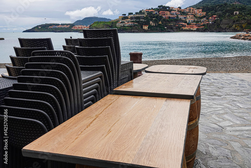 Obraz na płótnie Stacked black chairs line tables on a pier as waves lap at the shoreline. w salonie