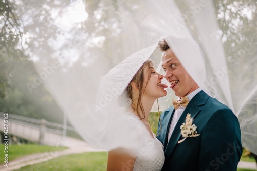 Bride and groom playfully stick out their tongues at each other under a veil. Fun and humorous wedding moment full of joy and personality..