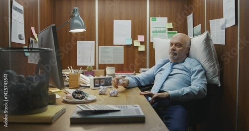 Bored inefficient employee sitting at his desk in a small office and wasting time