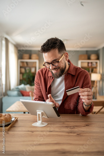 Happy man making online payment using tablet and credit card at home