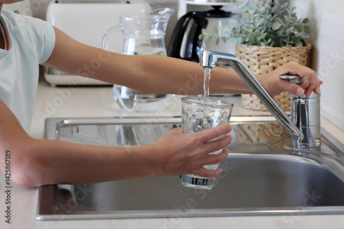 Kid's hands pouring a glass of clean water from the kitchen faucet on a sunny day