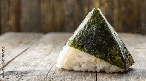 Obraz na płótnie A shot of a rice ball in the shape of a triangle, wrapped in seaweed and placed on a traditional wooden table, with soft light illuminating the details w salonie