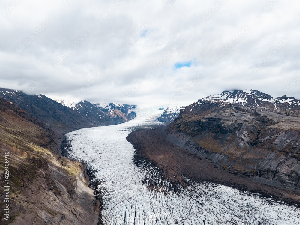 Aerial view of Vatnajökull glacier flowing through a steep valley surrounded by Icelandic mountains.