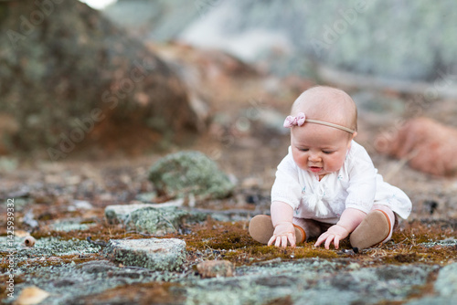 Baby girl sitting on ground touching moss