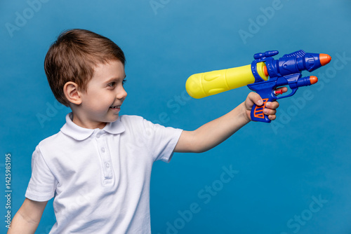 Laughing child boy playing with water gun toy on blue background. Pool toys and water fun for family with children. Summer vacation with kids. Active outdoor sport for preschooler