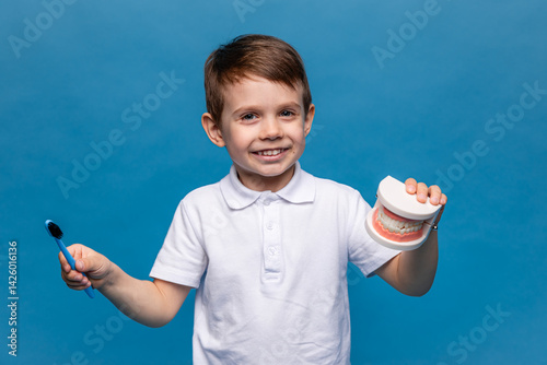 Obraz na płótnie Little boy holding tooth jaw, toothbrush on blue background. Kid training oral hygiene. Child learning brushing, cleaning teeth. Prevention of caries in children. children dentistry. dental care kids w salonie