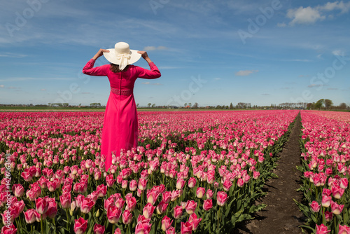 abstract portrait woman in long pink classic dress with white summer hat  standing in tulip flower field seen from behind for bookcover photo