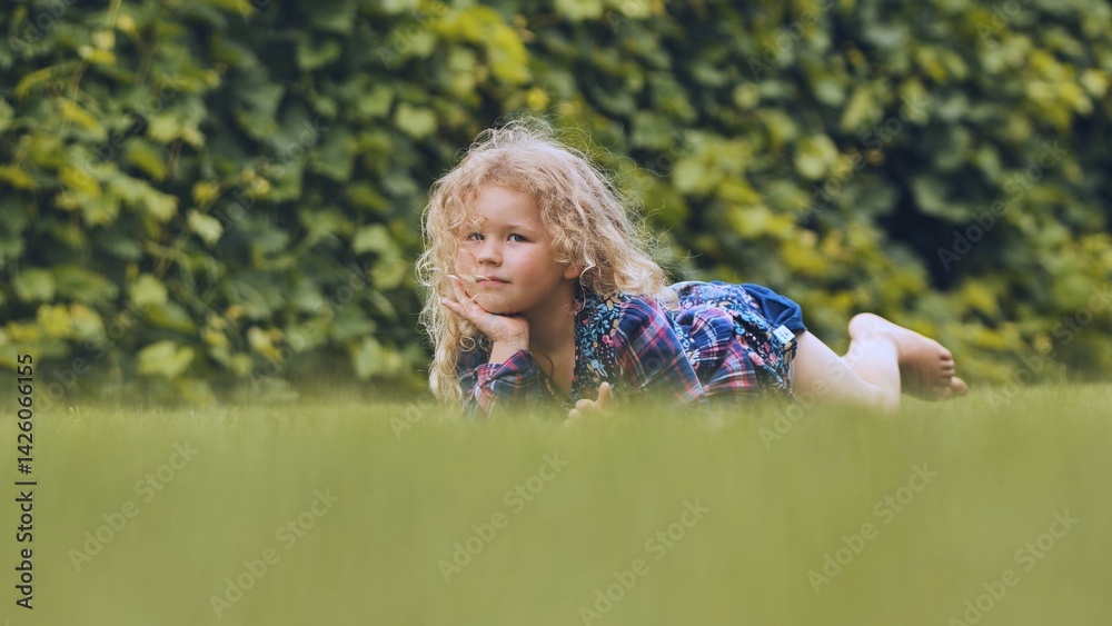 Obraz premium Blond girl reclining on verdant grass, basking in family moments amid natural park landscape, radiating carefree summer happiness