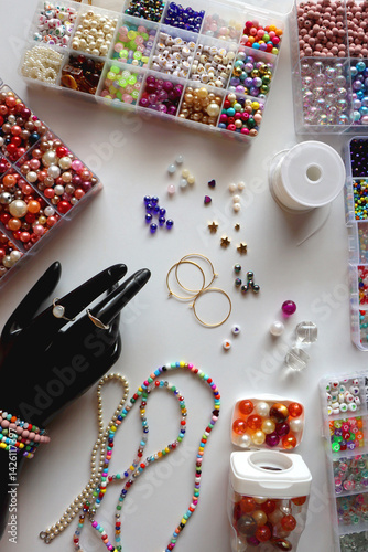 Obraz na płótnie Hand figurine, colorful friendship bracelets, necklaces, various beads and DIY supplies on the table. Making jewelry at home. Flat lay. w salonie