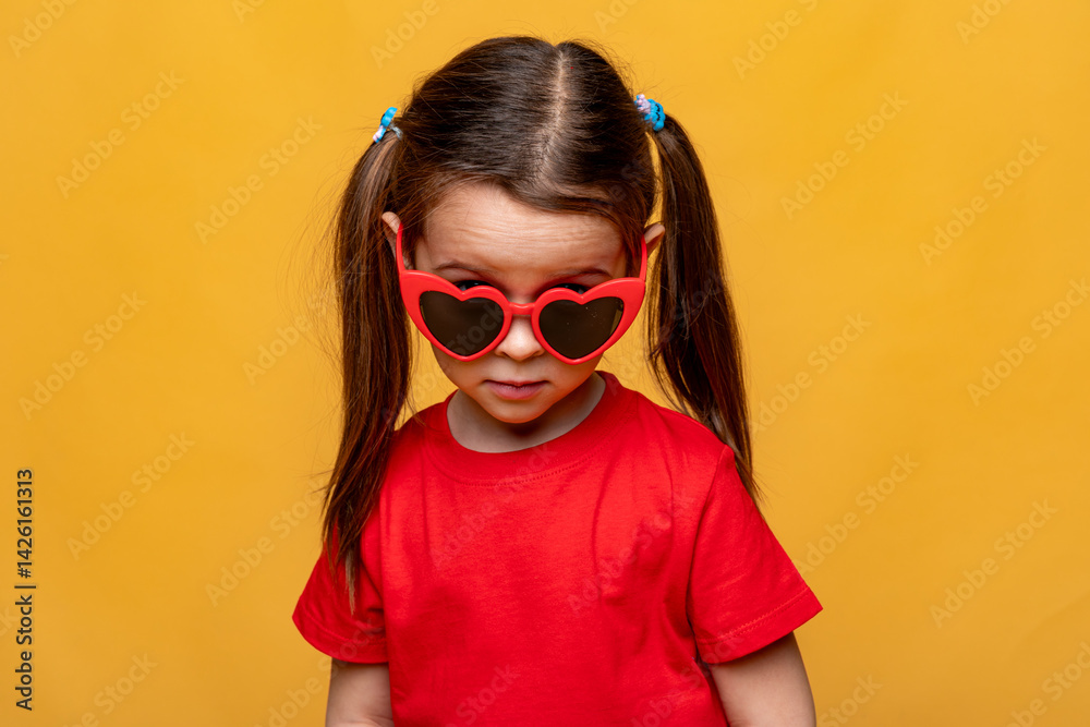 Smiling little child girl dressed in a red t-shirt and red funny sunglasses on yellow studio background. Summer travel vacation with children, advertising concept. Banner, mock up, copy space