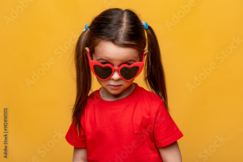 Obraz na płótnie Smiling little child girl dressed in a red t-shirt and red funny sunglasses on yellow studio background. Summer travel vacation with children, advertising concept. Banner, mock up, copy space w salonie