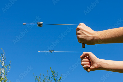 Modern dowsing with a metal L rods indicator in hands. Pair of Divining rods steel cylinder resonator for Bio location. An ancient method unproven by science