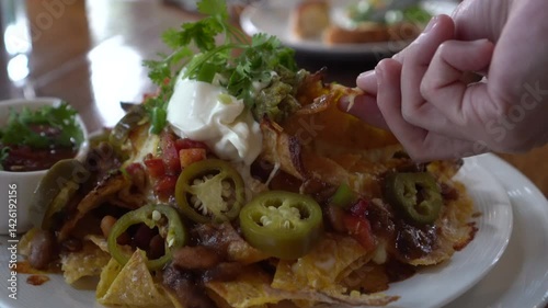 hand eating mexican food cheesy nachos plate with beef salsa jalapeno and sour cream