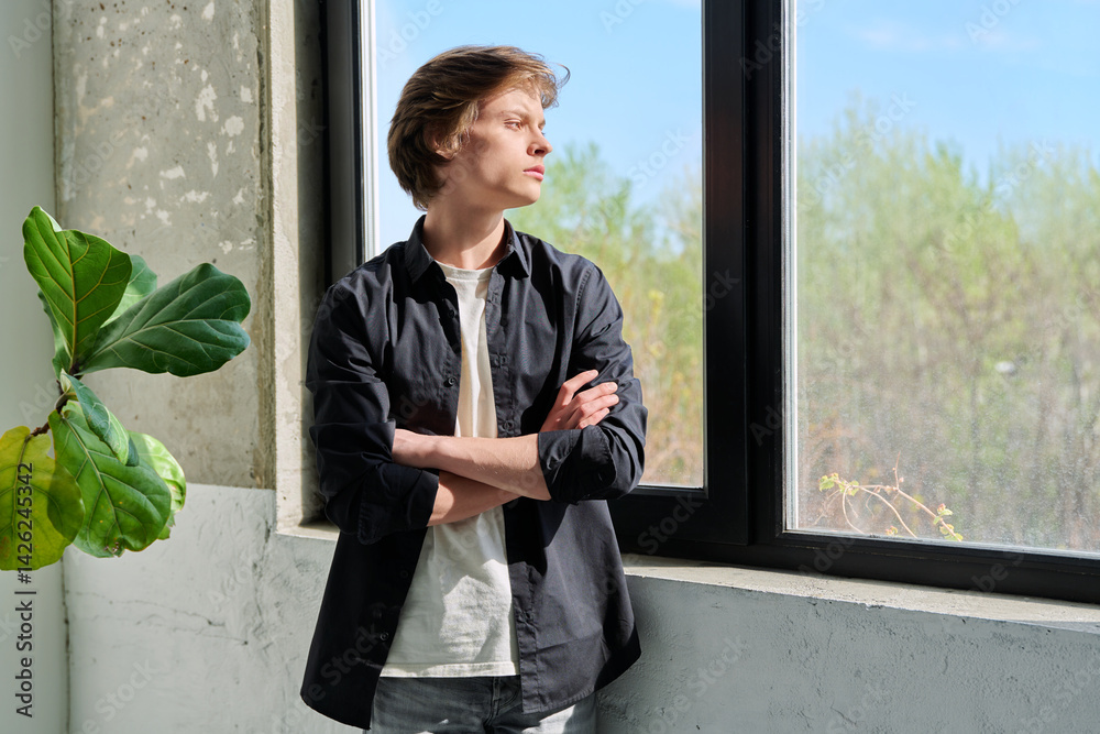 Upset sad teenager guy looking at window with crossed arms