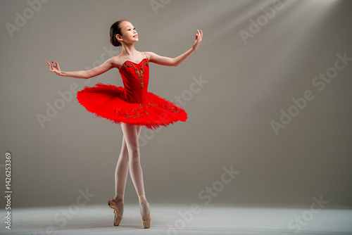 Young Japanese ballerina in red tutu and pointe shoes dances classical dance on light background.