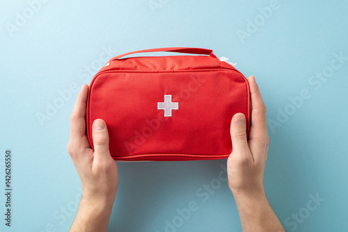 Photos Red first aid kit held by two hands on a clean light blue background showcasing