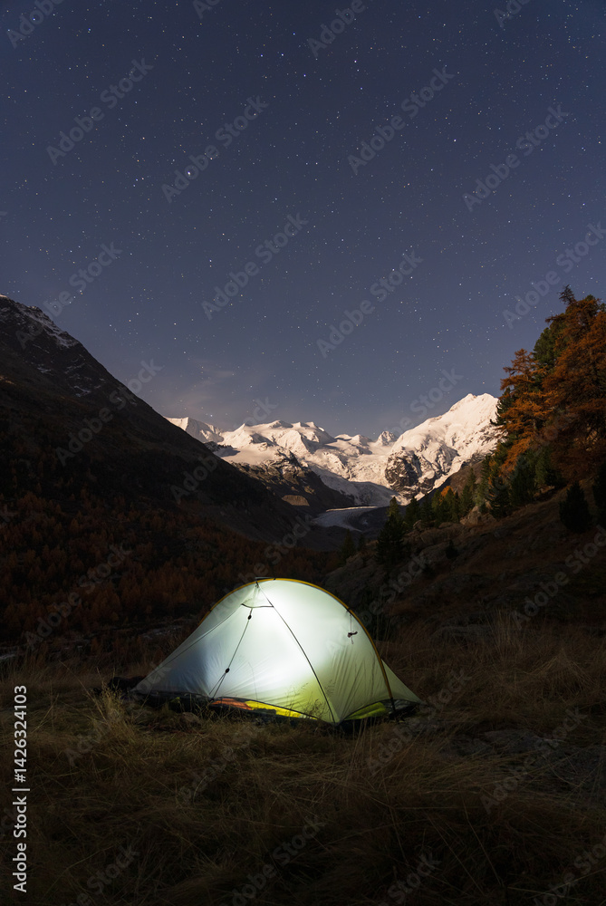 A tent under the night sky in the moonlit Bernina mountain group, Switserland.