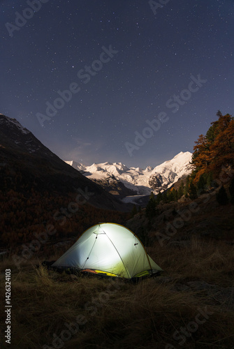 A tent under the night sky in the moonlit Bernina mountain group, Switserland.