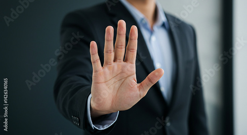 A person in a suit with an open hand gesturing stop in front of a dark background in a professional setting selling, purchasing, agreement, $