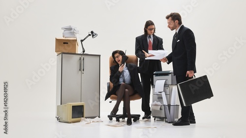 Fotografía Three office workers gathered around printer, woman yelling on phone while others present documents in messy white studio scene