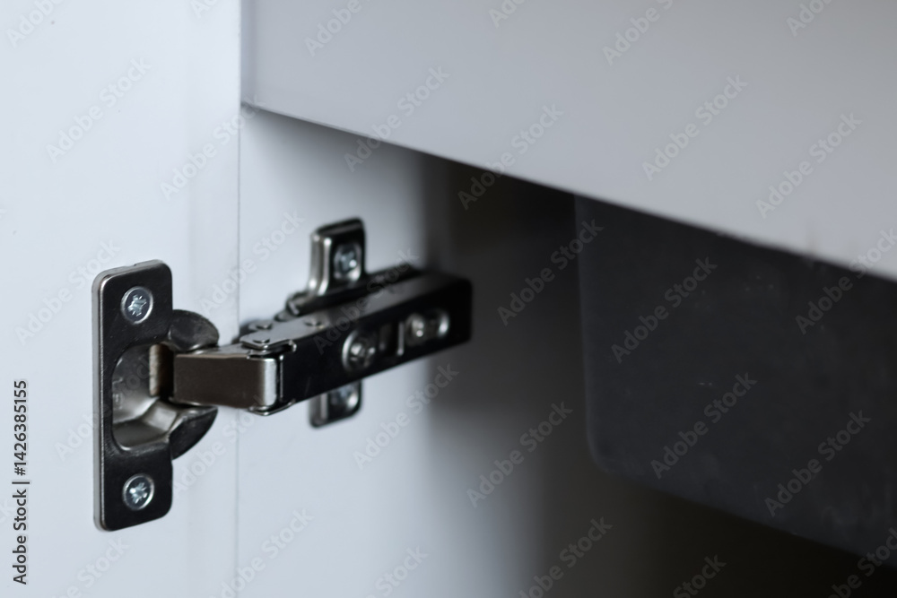 Close-up of kitchen cabinet hinge and accessories with white storage cabinet and sink in the background. perfect for home improvement, kitchen design, and modern storage solutions