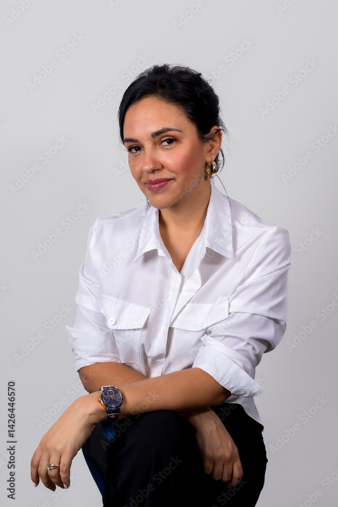 A woman is sitting on a chair and wearing a white shirt and black pants