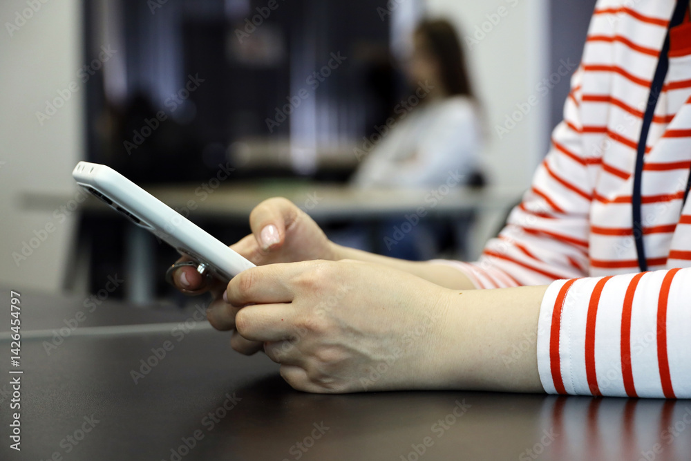 Smartphone in female hands, woman using mobile phone sitting at desk indoors