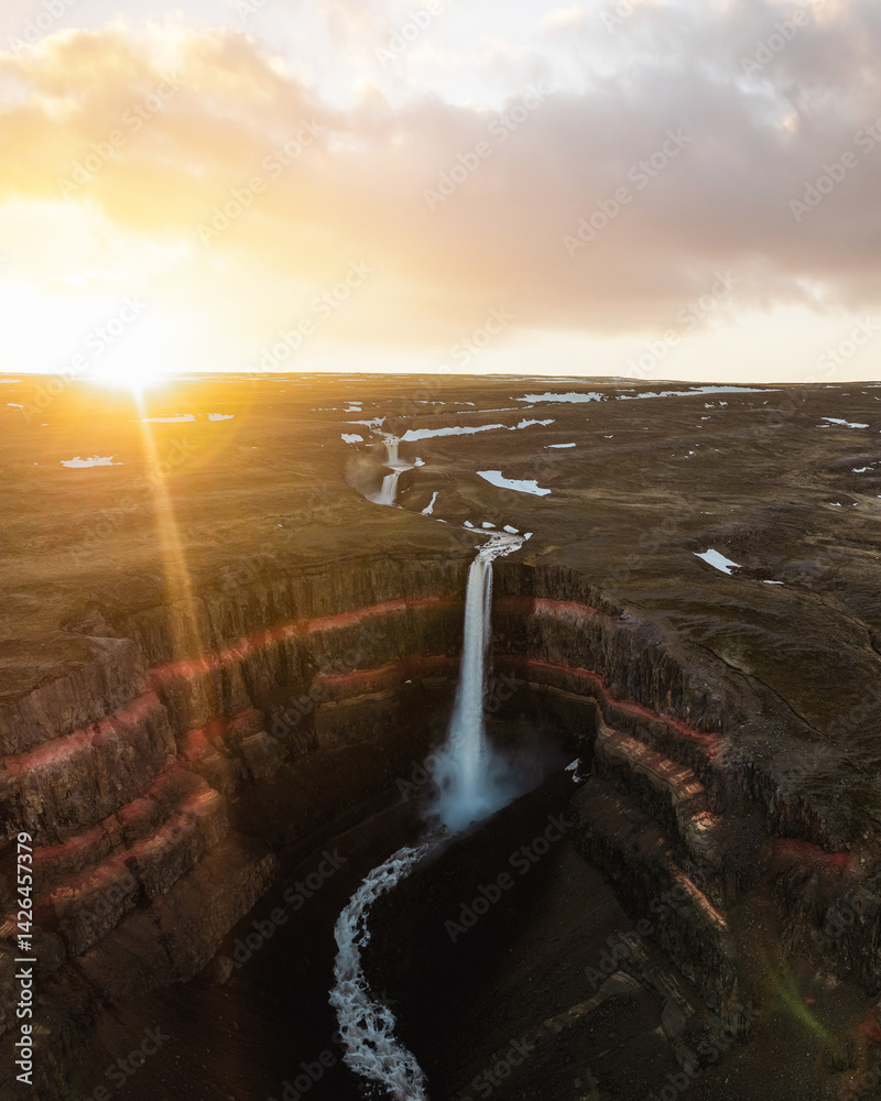 Aerial shot of Hengifoss waterfall at sunset, highlighting vivid red rock layers and dramatic cliffs in Iceland’s remote eastern highlands.
