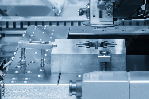 The die insert cutting process by wire EDM machine control by CNC program in the light blue scene. Closeup scene the wire EDM machine cutting the mold insert parts.