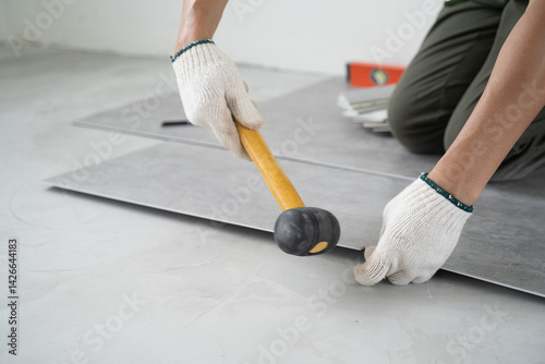 Close up of male worker using rubber hammer to install and adjust laminate flooring board. Man preparing laminate plank for floor installation in apartment under renovation.