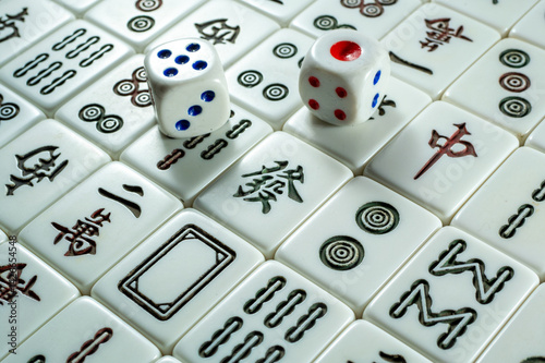 A close-up of Mahjong tiles with two dice placed on top, featuring symbols and characters in a traditional game setup.