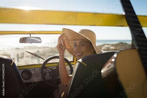 Принти на полотні woman sitting in yellow dune buggy at sandy beach, adjusting straw hat and reach