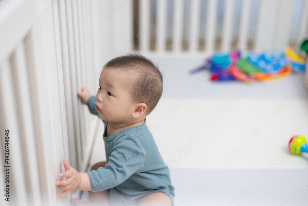 Baby touching white crib while sitting inside playpen