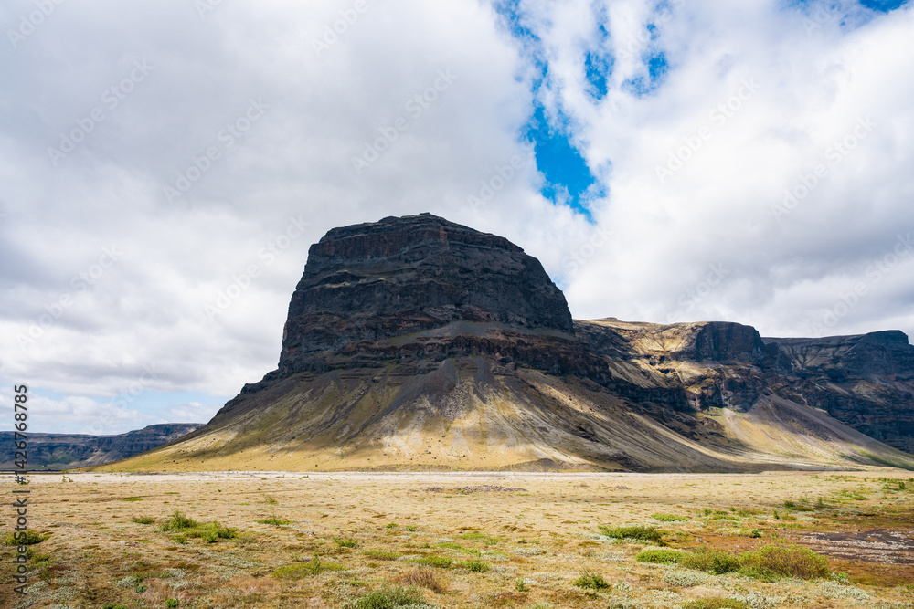 Isolated flat-topped mountain in Iceland under a dramatic sky, with golden slopes and tundra vegetation in the foreground.