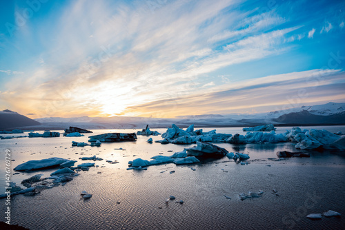 Blue glacial ice drifting in calm waters of an Icelandic lagoon, bathed in soft light with moody Arctic skies.
