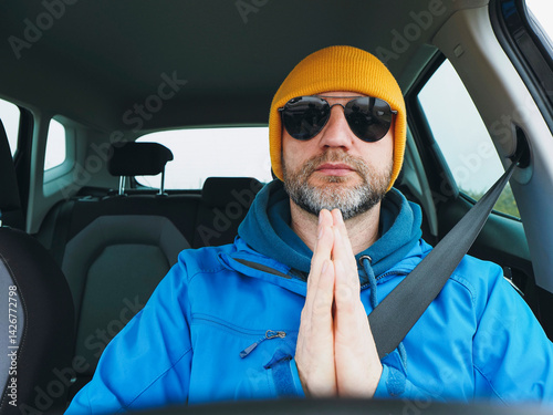 Obraz na płótnie Man driver in blue jacket and yellow hat wearing dark aviator glasses. Travel and transport. Male model with grey beard, hands in prey gesture. Road safety theme. w salonie