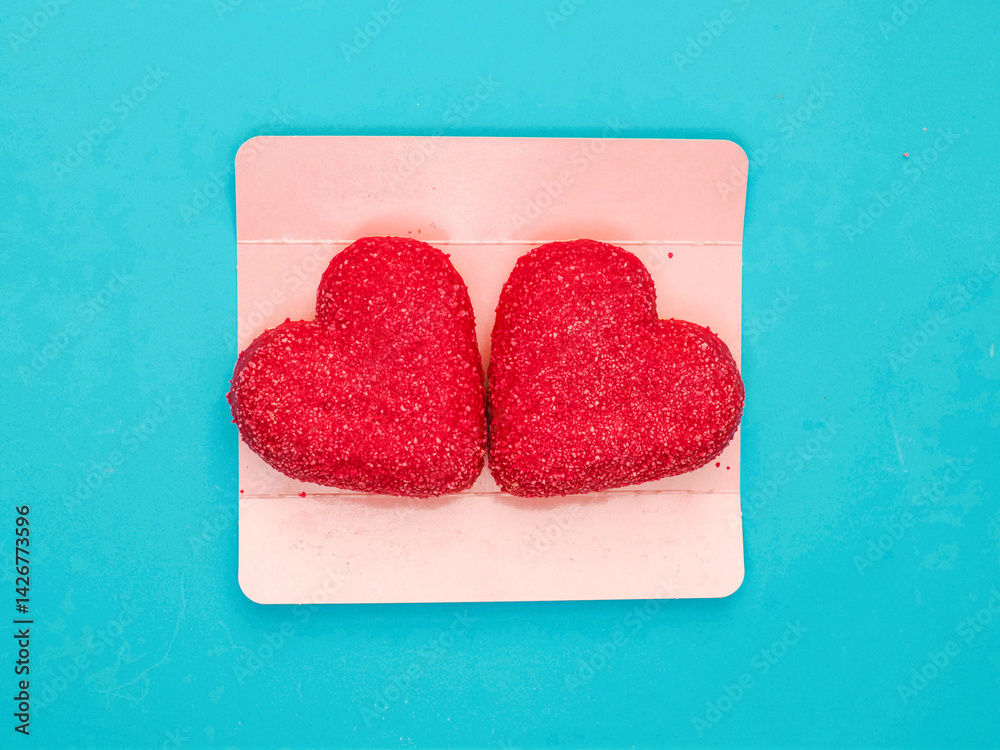 Two red heart shaped donuts on pink cardboard packaging for Valentine day or special event. Romantic expression of feeling through food. Fine bakery product. Blue background. Special couple treatment