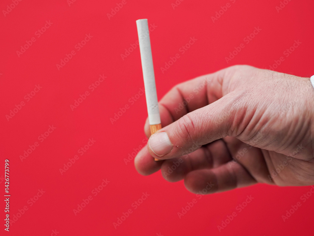 Hand holding a cigarette. Red color background shows danger of tobacco product consumption. Unhealthy habit.