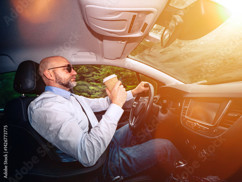 Obraz na płótnie A man in a white shirt and sunglasses is driving a car. He is wearing a tie and sunglasses, and the car is parked in a nature area with green trees. Unwind after hard working day concept. w salonie