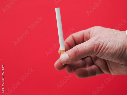 Obraz na płótnie Hand holding a cigarette. Red color background shows danger of tobacco product consumption. Unhealthy habit. w salonie
