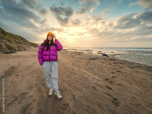 Obraz na płótnie Teenager girl walking on stunning Fanore beach in county Clare, Ireland. Travel and tourism concept. Blue ocean, dramatic sky and sun. Warm sunny day. Model wears purple jacket and grey pants. w salonie