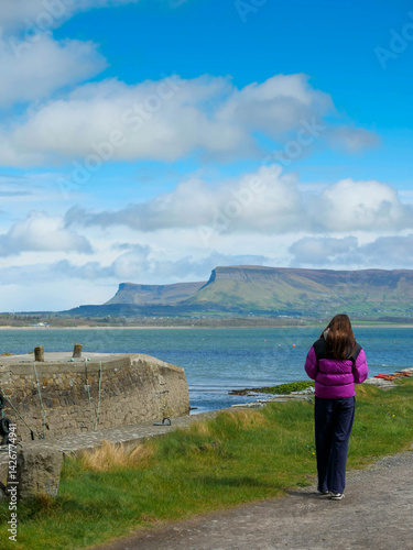 Obraz na płótnie Travel in Ireland. Girl tourist looking at stunning Benbulbin flat top mountain in county Sligo, Ireland. Warm day with rich blue cloudy sky. Amazing Irish nature scenery. Explore nature concept. w salonie