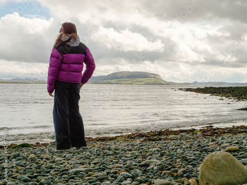 Obraz na płótnie Travel in Ireland. Young girl standing on rough stone beach and looking at ocean and Knocknarea mountain in the background. Stunning Irish nature. Cloudy sky. Famous landmark in county Sligo w salonie